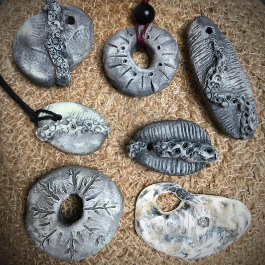 A selection of handcrafted grey and white pendants inspired by real fossil finds such as petrified sea urchins, barnacle-covered stones and ancient shells. Ideal as nautical necklaces or hatband adornments for sailors and wanderers.
