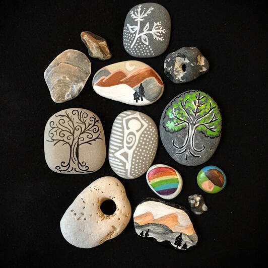 Natural stones painted with nature-inspired motifs like a mushroom, some hills under a half moon, and ornamental trees