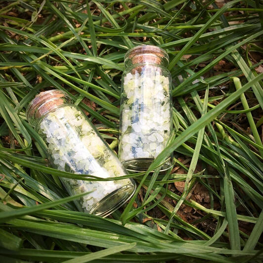Two small corked bottles with a greenish salt in it are lying in the green grass.